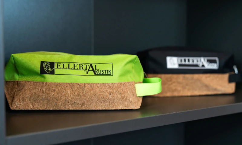 Zwei nachhaltige Kosmetiktaschen aus Kork und Stoff mit Ellertal Akustik Logo im Regal.
