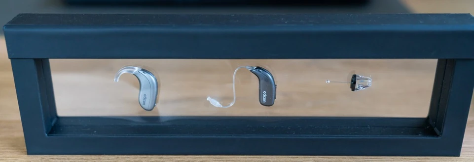 Moderne Hörgeräte verschiedener Bauarten in einem schwarzen Präsentationsrahmen ausgestellt.